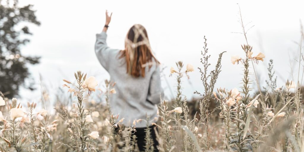 woman in a field of flowers praying the word of God with her hand lifted up